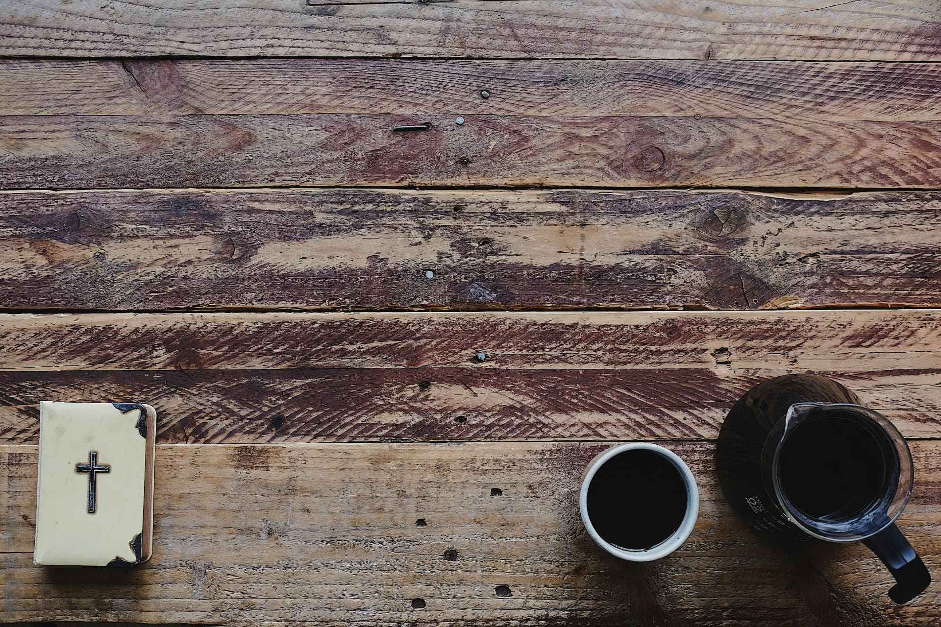 An open Bible and coffee on a weathered wooden table